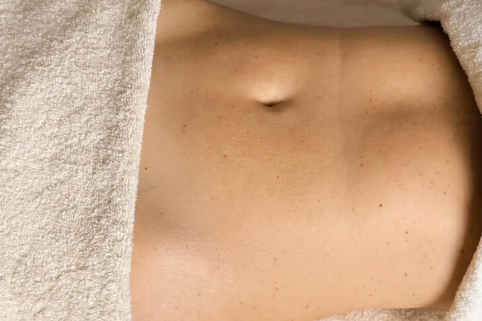 Abdomen avant chirurgie, drapé serviette blanche, ambiance cabinet paramédical.